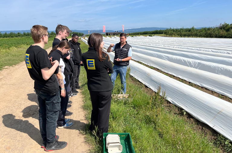 Juniorchef Björn Hochhaus erläutert den interessierten EDEKA-Deckenbach-Azubis direkt am Spargelfeld die Anabuamethoden