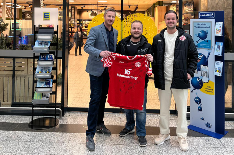 Marktinhaber Klaus Deckenbach (links) mit dem glücklichen Gewinner Herrn Presper und Herrn Laws (rechts) vom 1. FSV Mainz 05 bei der Übergabe des signierten Trikots vor dem Markteingang in Hartenberg